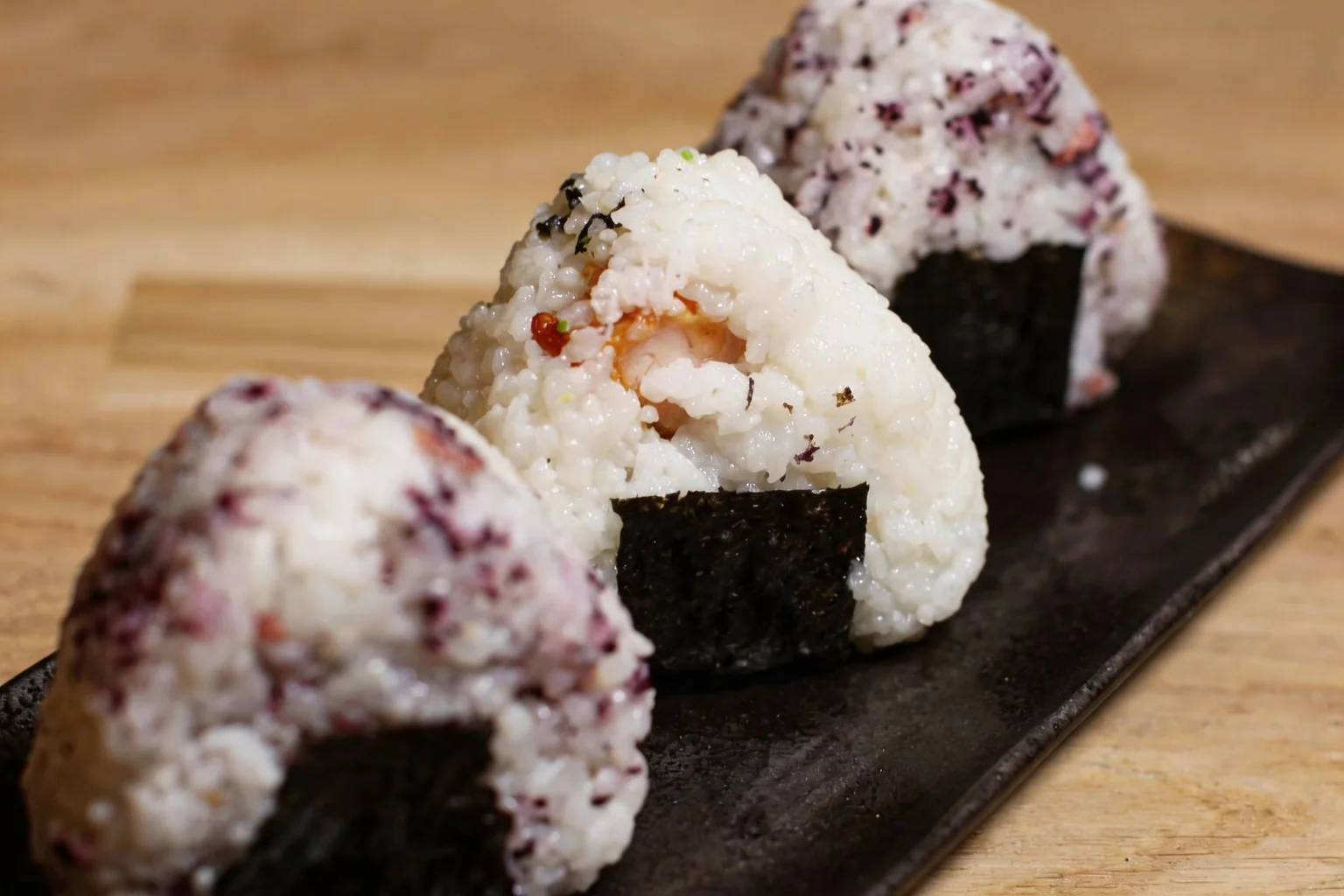 Onigiri on a long black plate, wooden table.